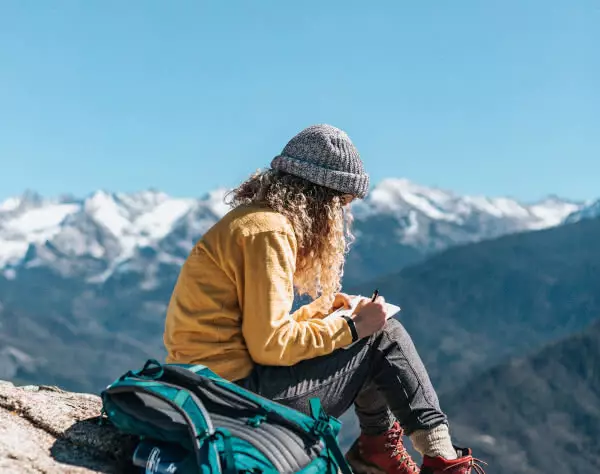 Online freelance journalism course student writing on top of a mountain